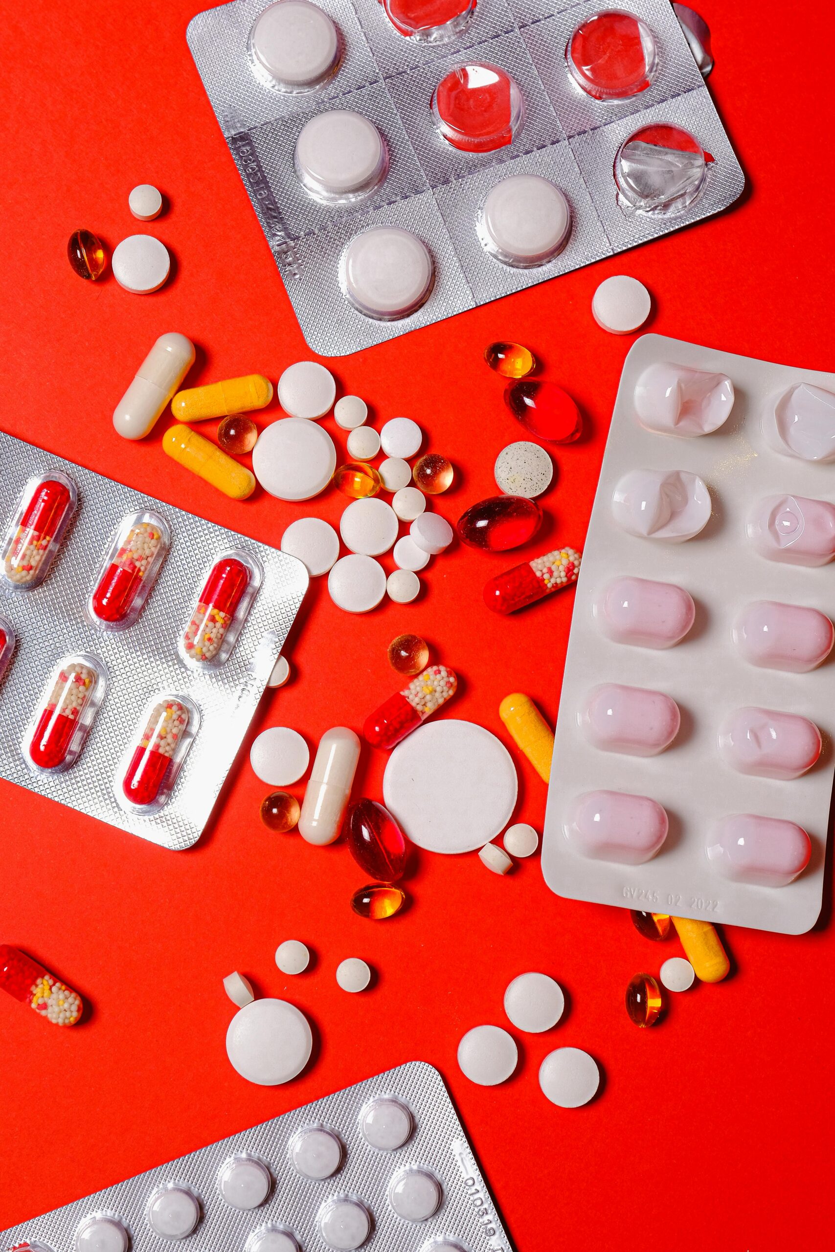 A close-up of various pills and capsules on a vibrant red background, highlighting healthcare and medicine.