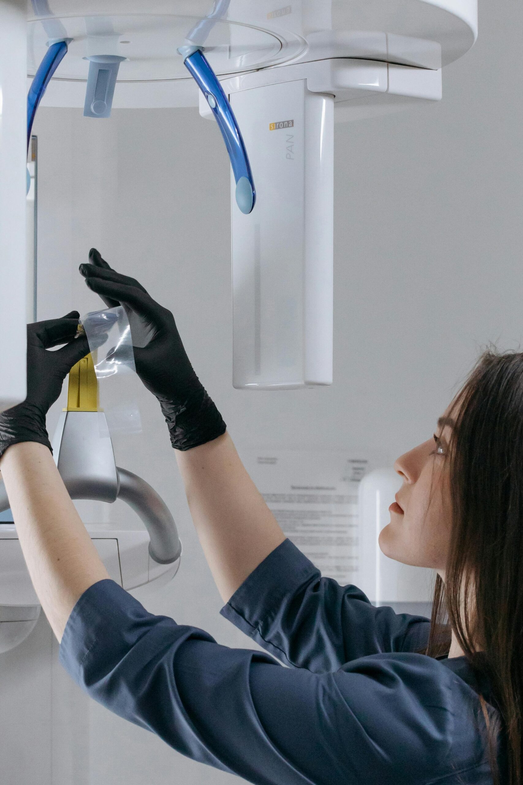 Dental technician with black gloves adjusting dental x-ray machine in clinic.