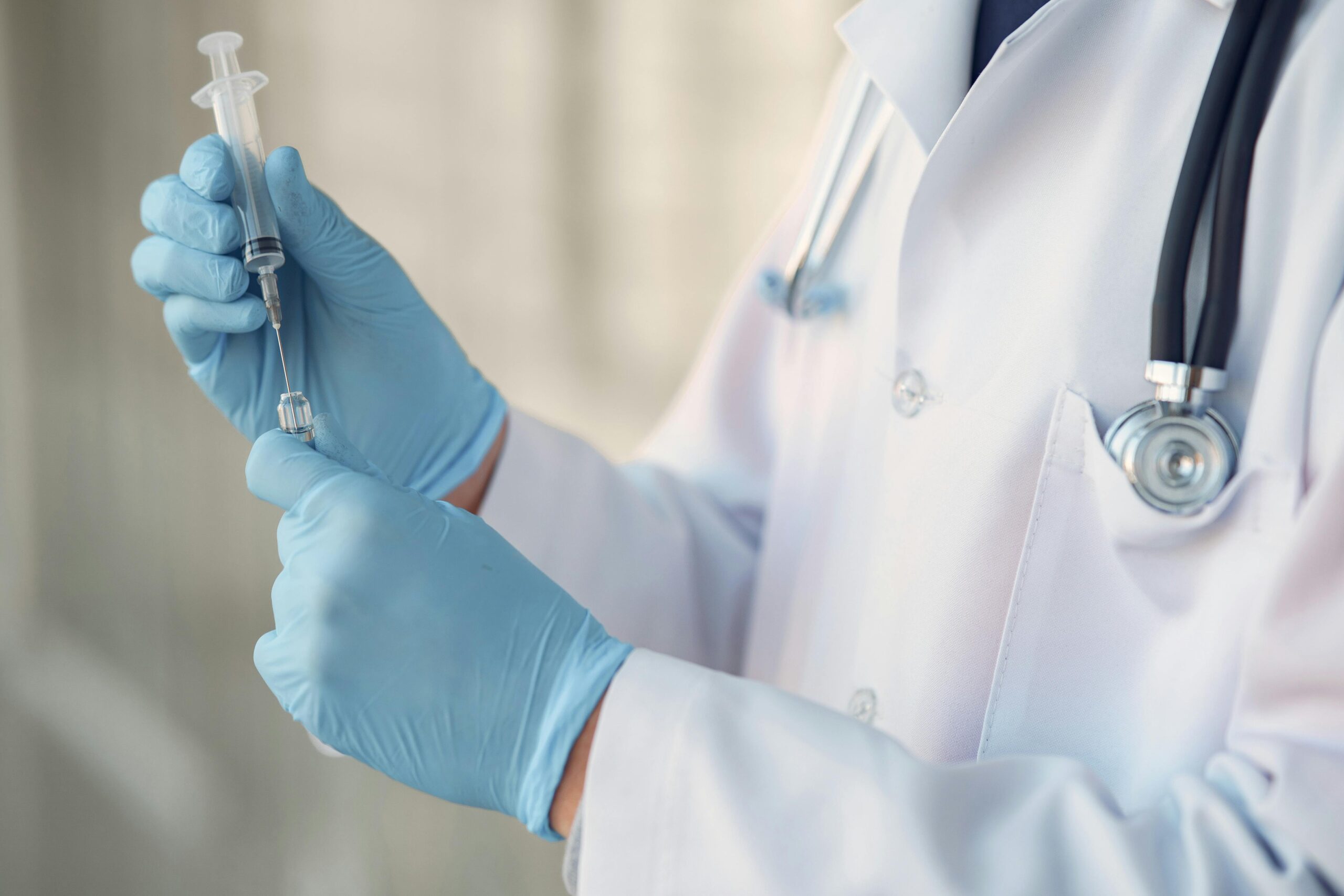 Healthcare professional wearing gloves and holding a syringe in a clinical setting.
